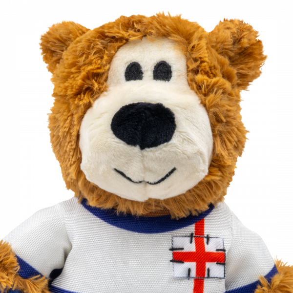 KONG Wild Knots World Cup England Bear Close Up 1080px A detailed close-up shot of the KONG Wild Knots England Bear's face and upper chest. The bear features an off-white muzzle, a large black plush nose, and small stitched eyes that are safe for pets. The St George’s Cross patch on the white football shirt is clearly visible with detailed black "stitch" accents. The image showcases the high-quality, shaggy brown plush fabric used throughout the toy.
