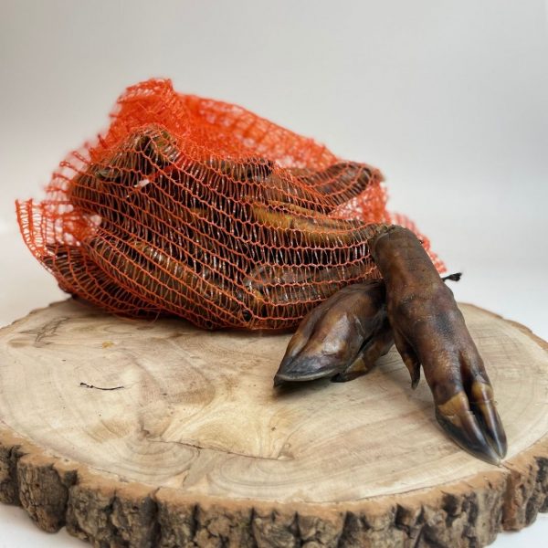 Wild Boar Trotters net on log A bulk pack of Wild Boar Trotters natural dog chews in orange netting on a rustic log - MAH Pet Supplies
